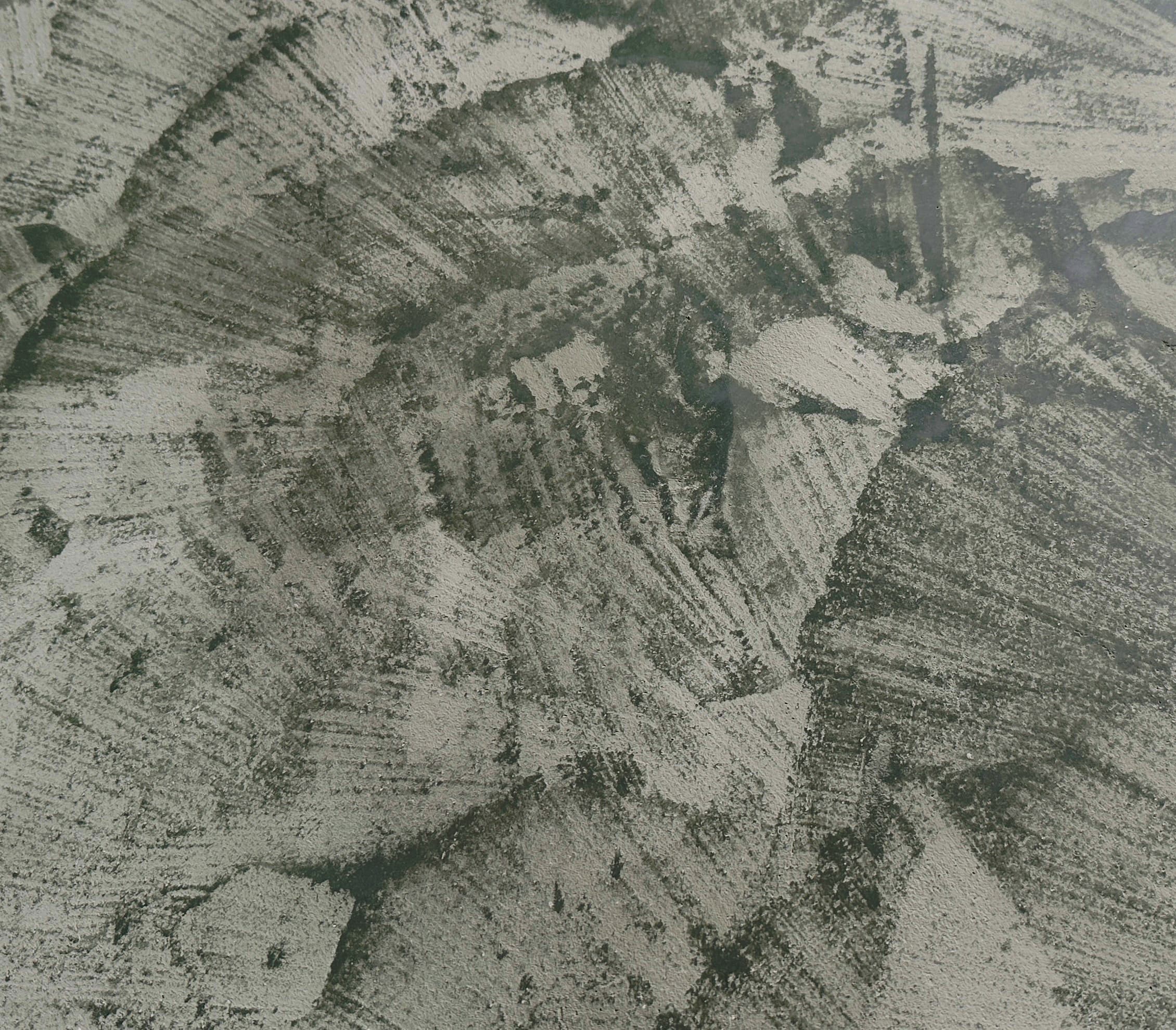 A charcoal lime-plaster surface, fanned trowel strokes sweeping across it and catching a fine mineral speckle.