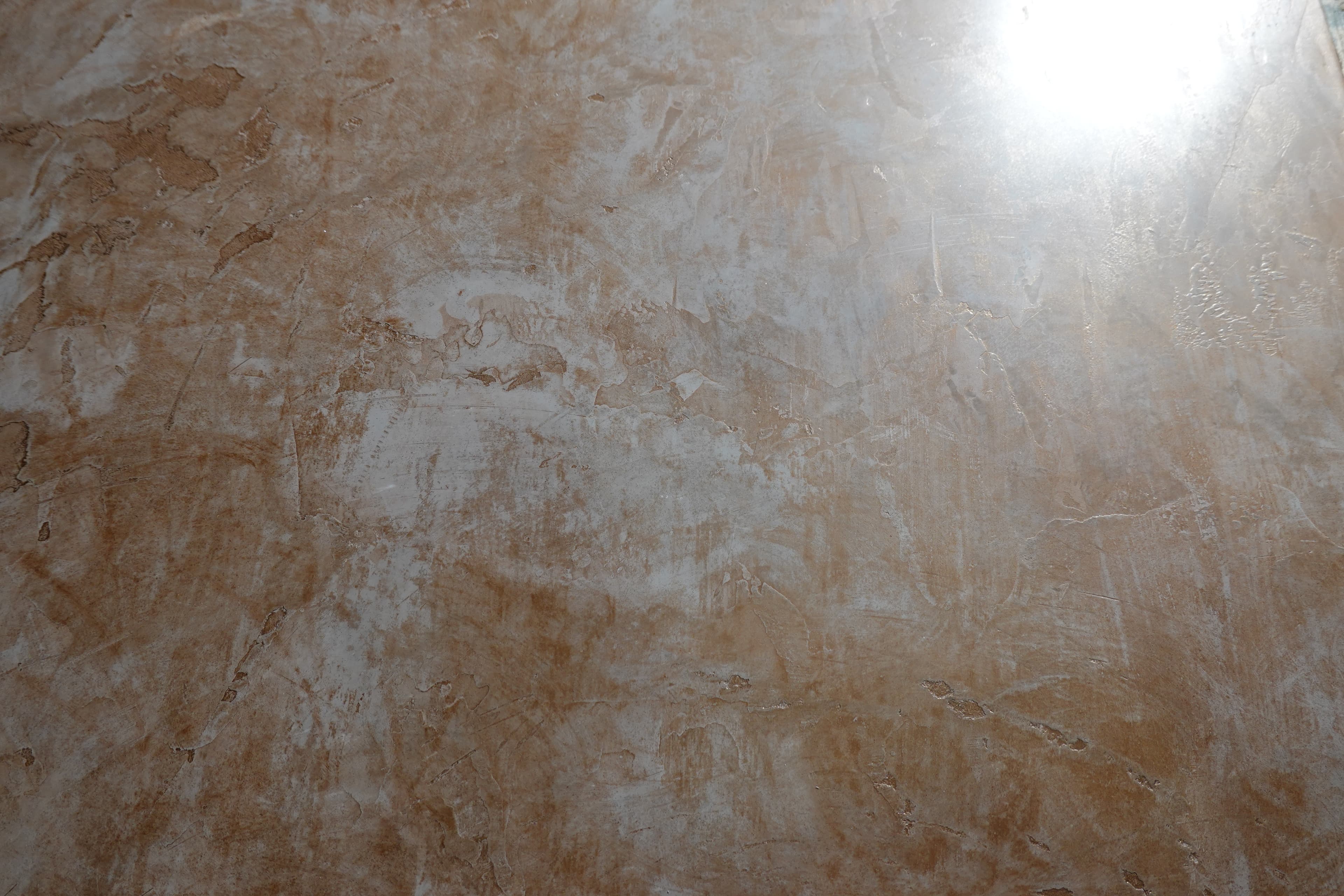 A close view of a terracotta lime-plaster surface, pale cloud-like passages drifting through it and light raking off the burnish.